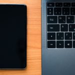 Notebook e smartphone lado a lado sobre uma mesa de madeira, representando a integração entre dispositivos tecnológicos.