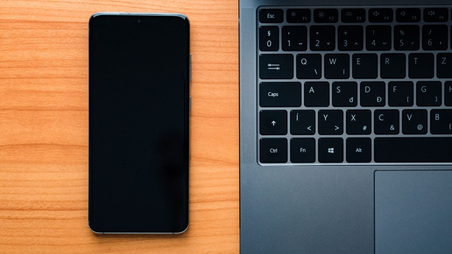 Notebook e smartphone lado a lado sobre uma mesa de madeira, representando a integração entre dispositivos tecnológicos.