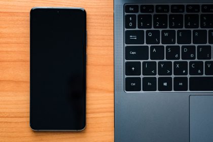 Notebook e smartphone lado a lado sobre uma mesa de madeira, representando a integração entre dispositivos tecnológicos.