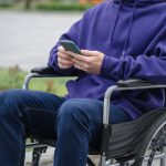 Pessoa em cadeira de rodas usa um smartphone ao ar livre.