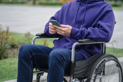 Pessoa em cadeira de rodas usa um smartphone ao ar livre.