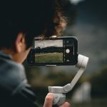 Pessoa usando um smartphone montado em um gimbal para filmar uma paisagem ao ar livre.