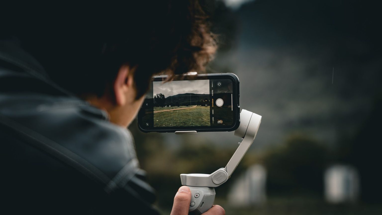 Pessoa usando um smartphone montado em um gimbal para filmar uma paisagem ao ar livre.