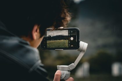 Pessoa usando um smartphone montado em um gimbal para filmar uma paisagem ao ar livre.