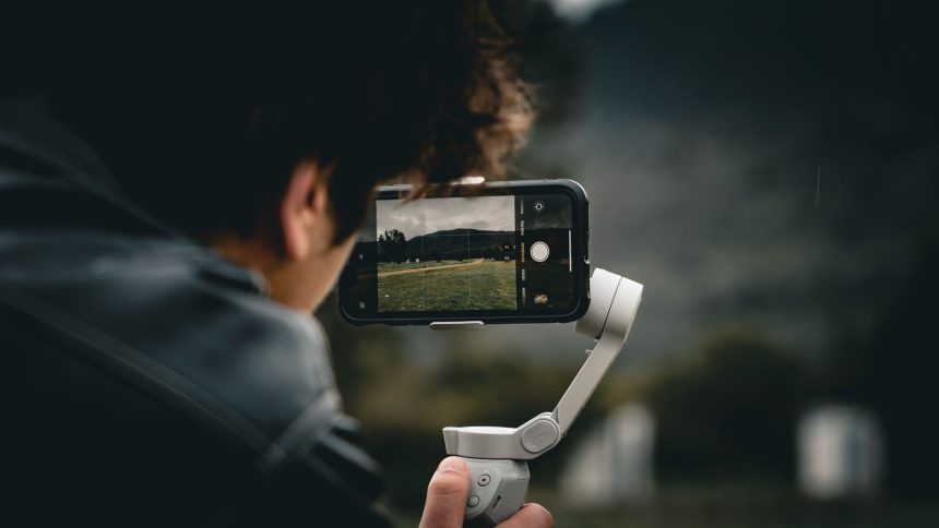 Pessoa usando um smartphone montado em um gimbal para filmar uma paisagem ao ar livre.