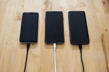 Três smartphones conectados a carregadores sobre uma superfície de madeira.