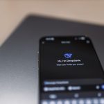 Smartphone exibindo uma interface de assistente de inteligência artificial sobre um laptop.
