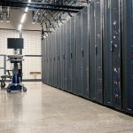 Armários metálicos com servidores, dispositivos de rede e cabos em um datacenter moderno.