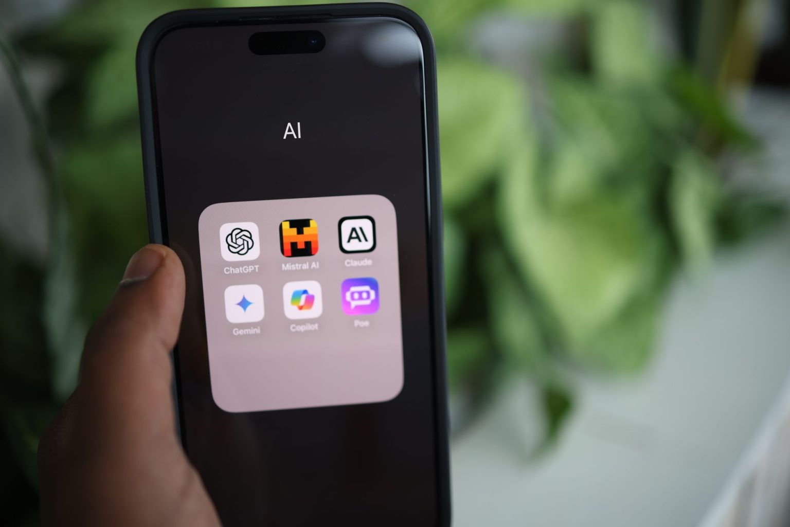 Smartphone exibindo aplicativos de inteligência artificial sobre um laptop, em uma composição com plantas ao redor