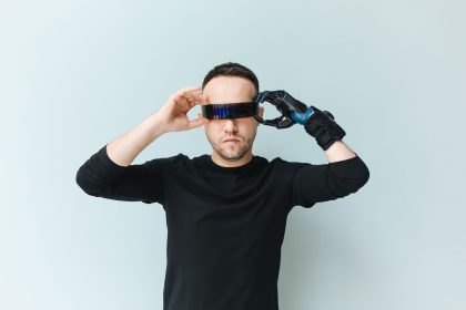 Homem ajusta óculos escuros de aparência futurista diante de um fundo neutro.