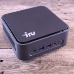 Computador compacto sobre uma mesa de madeira, com portas USB-C e outras conexões visíveis.