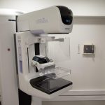 Equipamento de mamografia em ambiente hospitalar, acompanhado por uma profissional de saúde.