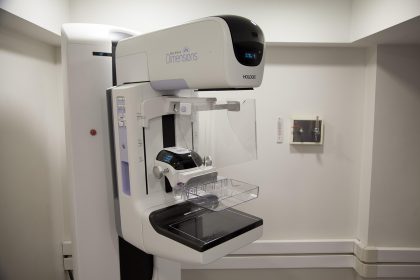 Equipamento de mamografia em ambiente hospitalar, acompanhado por uma profissional de saúde.